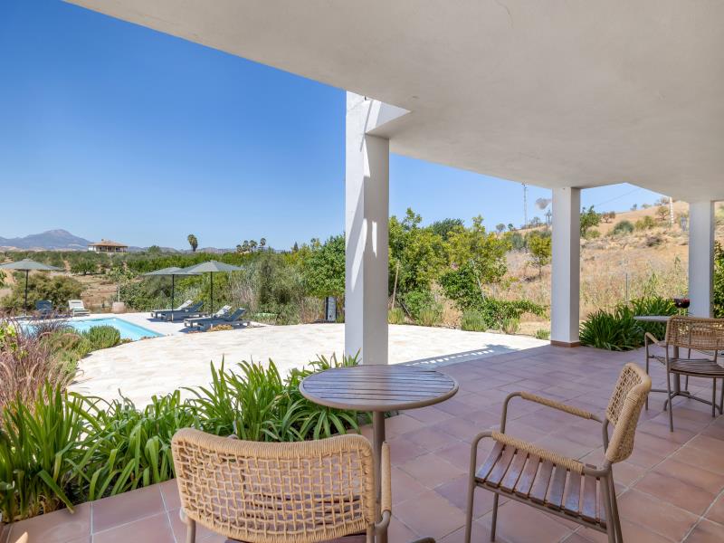 Covered terrace with dining table overlooking the pool and distant village