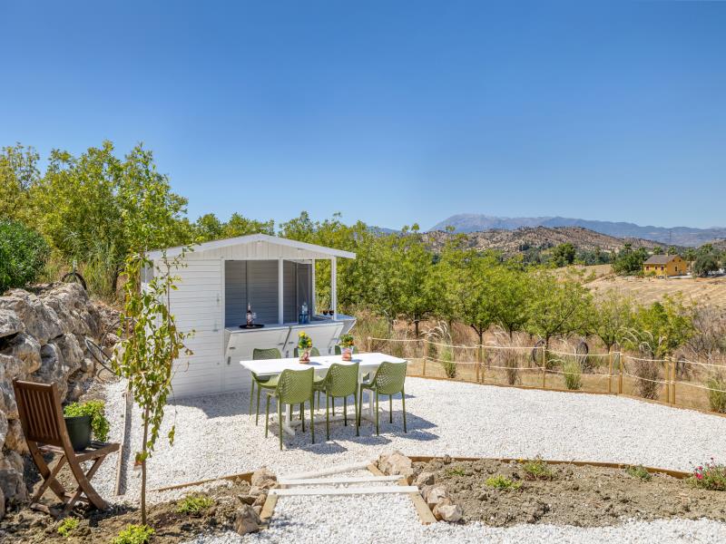 Outdoor kitchen with bar and long dining table on white gravel with mountain views