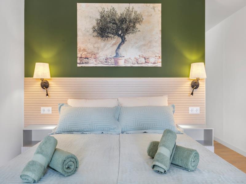Bed in room 3 with olive-tree artwork and rolled towels